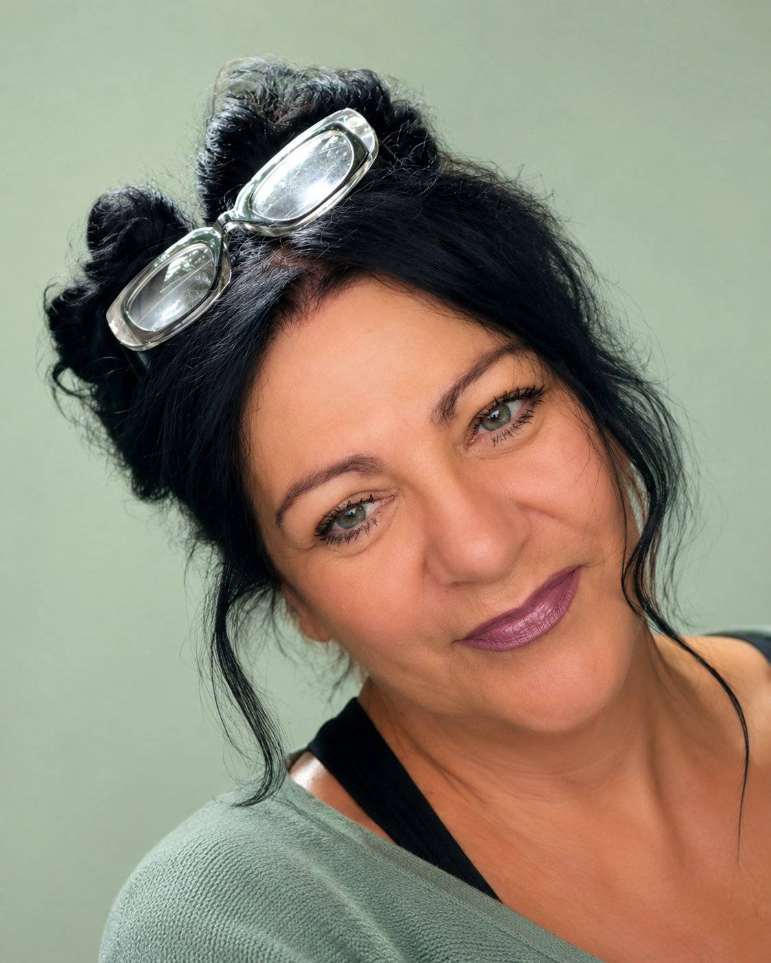Andrea Schäfer, Heilpraktikerin für Psychotherapie und systemische Familienaufstellung, lächelt in die Kamera – schwarze Hochsteckfrisur, Brille im Haar, salbeigrüner Hintergrund