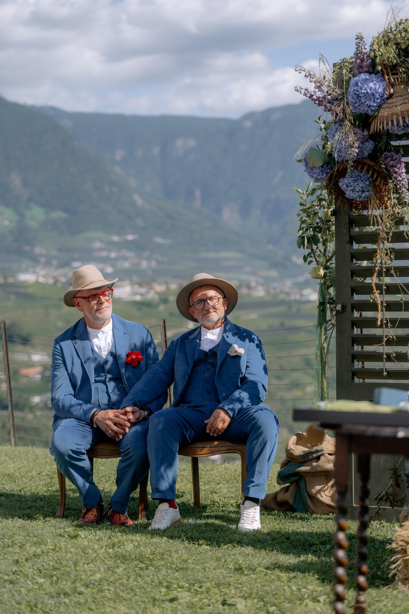 Thorsten Rausch und Ingmar Laimer sitzen bei ihrer freien Trauung unter dem Blumenbogen mit Blick über das Südtiroler Etschtal