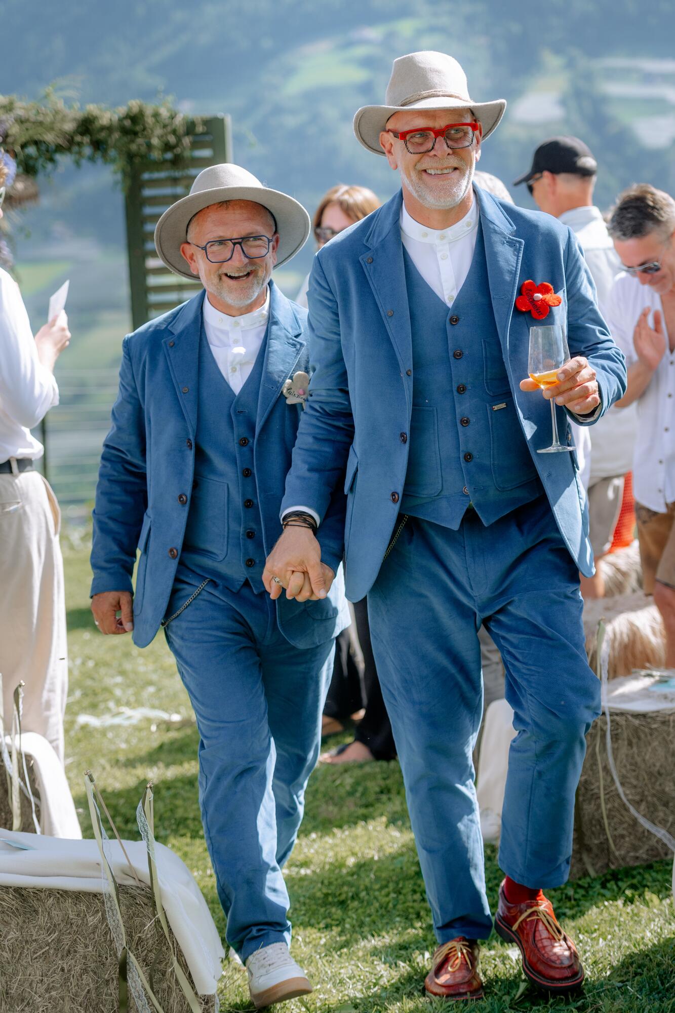 Thorsten Rausch und Ingmar Laimer gehen nach der Trauung lachend Hand in Hand durch ihre Hochzeitsgesellschaft