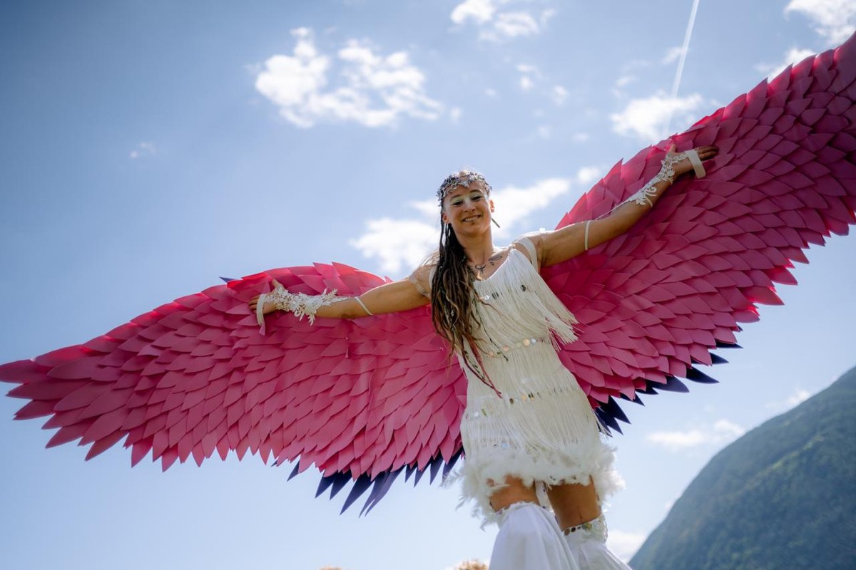 Walkact Zaubervogel von Firedancer mit pinken Flügeln auf Stelzen, Showkunst, Kooperationspartner vom Hof alla Cava